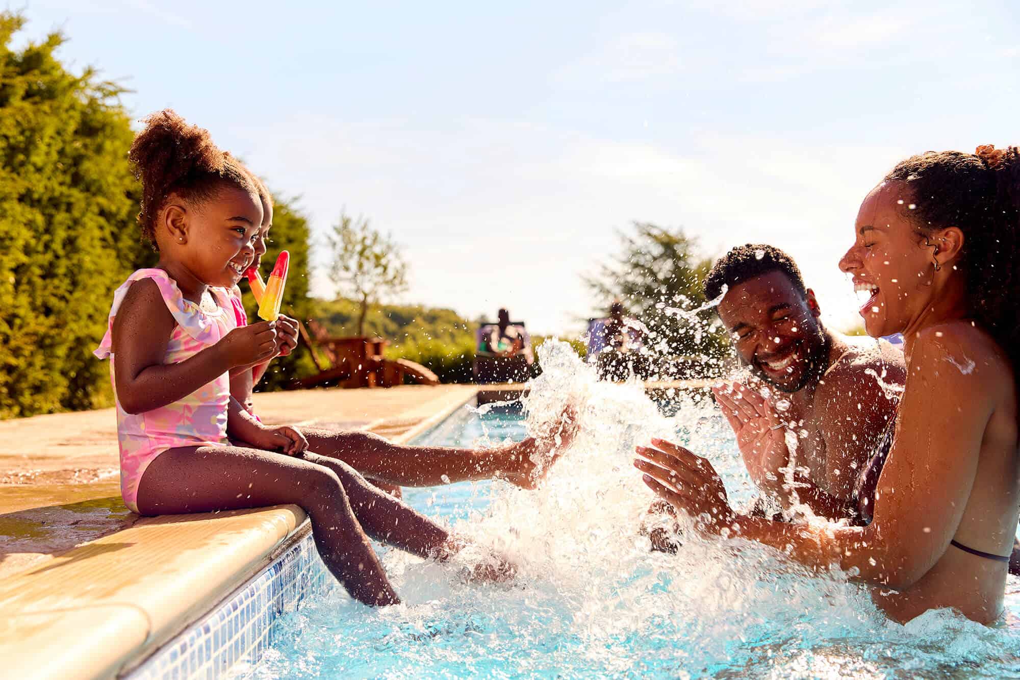 Small girl splashing feet at her parents while sitting on pool side